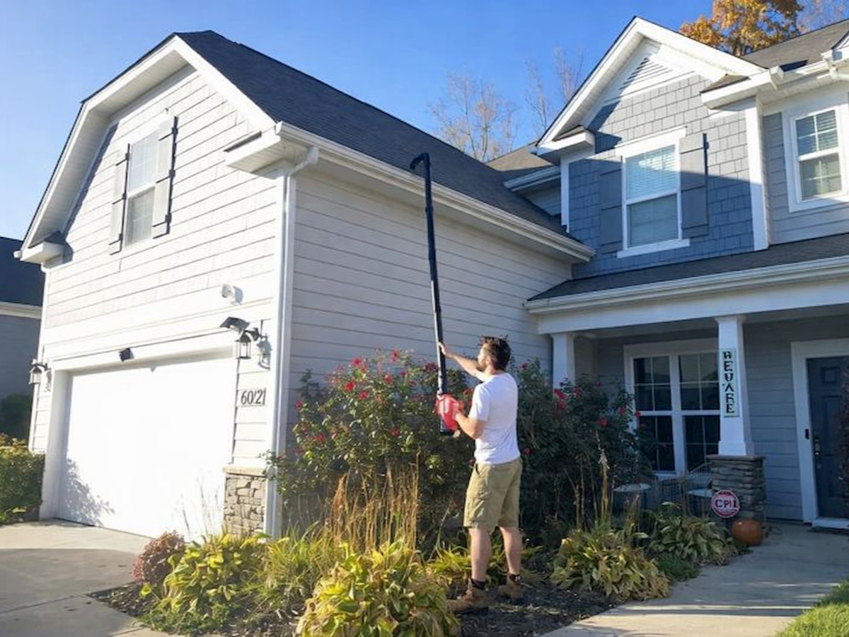 a man is cleaning the gutter from the ground using a gutter cleaner
